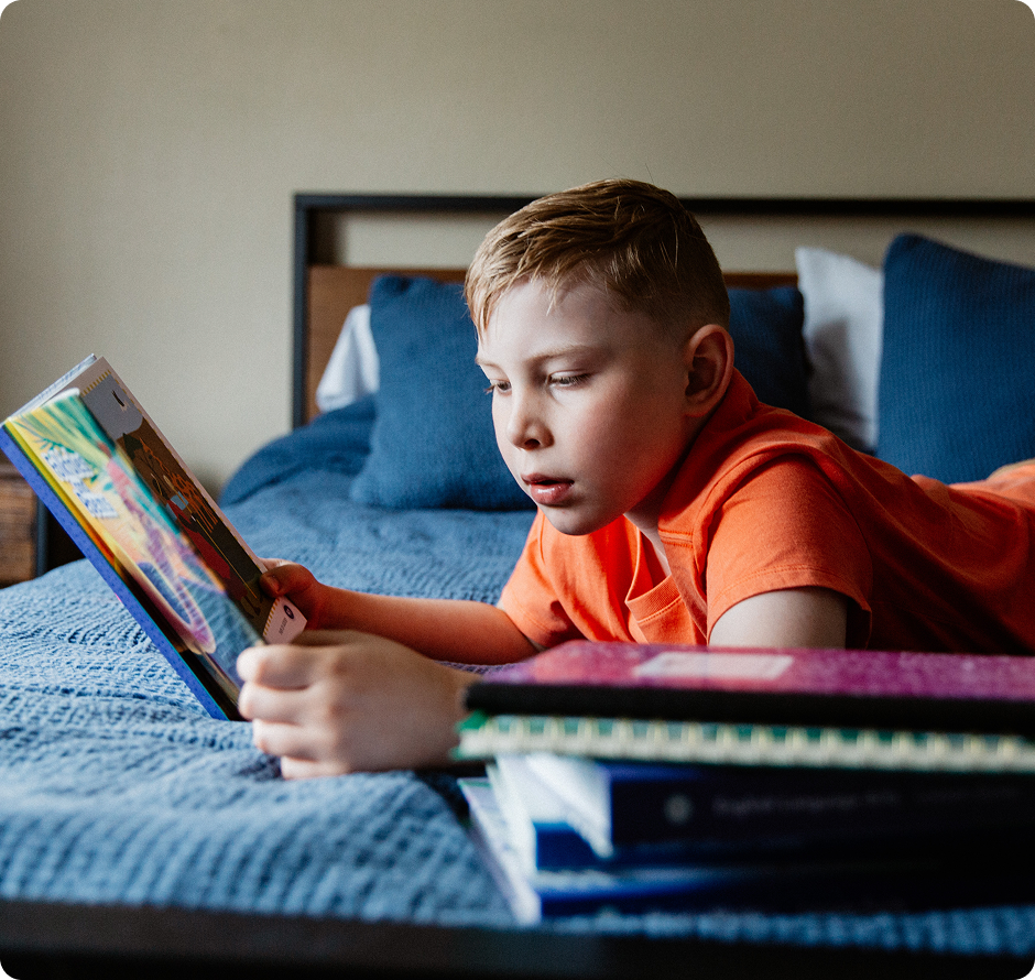 Elementary student reading a book in his bed